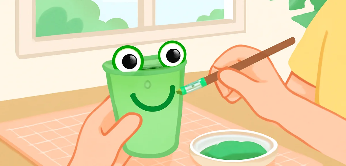 Child's hands decorating a paper cup to look like a frog with green paint and googly eyes on a craft